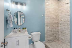 Bathroom with tiled shower, vanity, and toilet