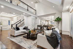 Living room with high vaulted ceiling, wood-type flooring, a notable chandelier, and ornamental molding