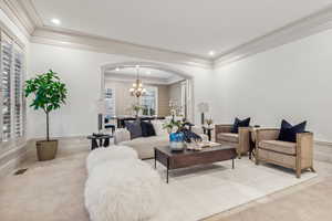 Carpeted living room with crown molding, plenty of natural light, and a chandelier