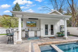 Exterior space featuring french doors, beverage cooler, exterior kitchen, a pool with hot tub, and a wet bar