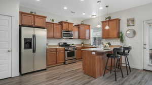 Kitchen with appliances with stainless steel finishes, decorative light fixtures, light hardwood / wood-style flooring, and a breakfast bar area