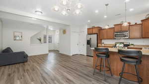 Kitchen with light stone countertops, a breakfast bar, stainless steel appliances, pendant lighting, and hardwood / wood-style flooring