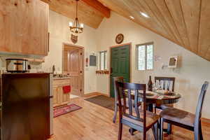 Dining space with vaulted ceiling with beams, wooden ceiling, light hardwood / wood-style floors, and a notable chandelier