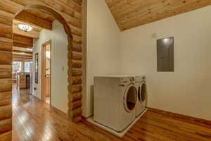 Laundry room featuring washing machine and clothes dryer, log walls, light hardwood / wood-style flooring, electric panel, and wood ceiling