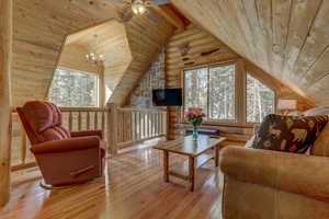 Living room featuring lofted ceiling with beams, light wood-type flooring, ceiling fan with notable chandelier, and wooden ceiling