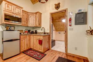 Kitchen featuring sink, stainless steel microwave, vaulted ceiling, fridge, and light wood-type flooring