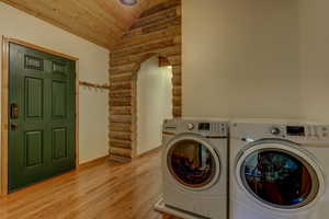 Washroom with rustic walls, wooden ceiling, washer and dryer, and light hardwood / wood-style floors