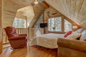 Bedroom with vaulted ceiling with beams, ceiling fan with notable chandelier, wood-type flooring, and wooden ceiling