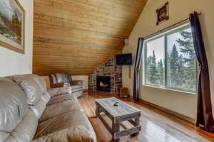 Living room featuring a stone fireplace, wood ceiling, light hardwood / wood-style flooring, and vaulted ceiling