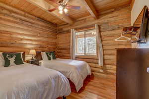 Bedroom with wooden ceiling, light hardwood / wood-style flooring, ceiling fan, rustic walls, and beamed ceiling