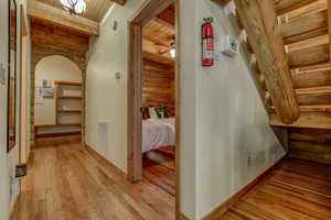 Corridor with beam ceiling, wood ceiling, rustic walls, and light hardwood / wood-style flooring