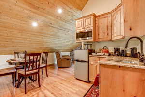 Kitchen with vaulted ceiling, sink, wooden ceiling, light hardwood / wood-style floors, and stainless steel microwave