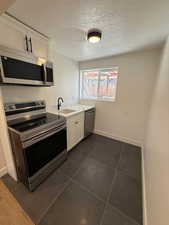 Kitchen featuring white cabinetry, sink, dark tile patterned floors, a textured ceiling, and appliances with stainless steel finishes