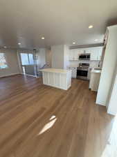 Kitchen with white cabinets, appliances with stainless steel finishes, a textured ceiling, a kitchen island, and light wood-type flooring