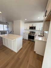 Kitchen with a center island, sink, hardwood / wood-style flooring, appliances with stainless steel finishes, and white cabinetry