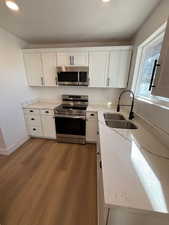 Kitchen featuring white cabinets, sink, light wood-type flooring, light stone counters, and stainless steel appliances