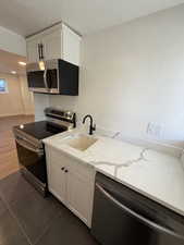 Kitchen with light stone countertops, white cabinetry, sink, and stainless steel appliances