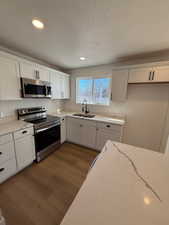 Kitchen featuring appliances with stainless steel finishes, light stone counters, sink, light hardwood / wood-style flooring, and white cabinets