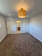 Unfurnished bedroom with a textured ceiling, connected bathroom, light colored carpet, and multiple closets