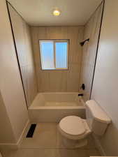 Bathroom with tile patterned flooring, tiled shower / bath combo, toilet, and a textured ceiling