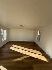 Unfurnished room with a textured ceiling, dark wood-type flooring, and lofted ceiling