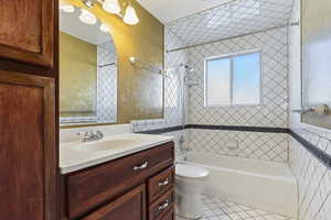 Full bathroom featuring vanity, tile patterned floors, tiled shower / bath, toilet, and tile walls