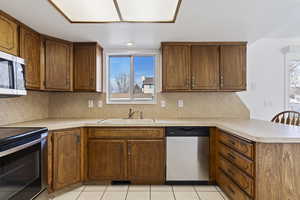 Kitchen with sink, stainless steel appliances, backsplash, kitchen peninsula, and light tile patterned floors