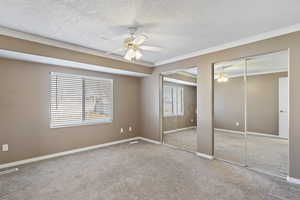 Unfurnished bedroom with ceiling fan, crown molding, a textured ceiling, carpet, and two closets