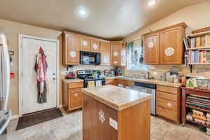 Kitchen with a textured ceiling, stainless steel appliances, vaulted ceiling, sink, and a center island