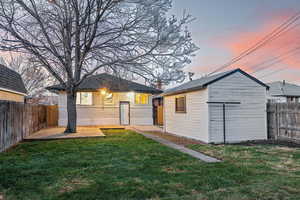 Back house at dusk with a lawn and an outdoor structure