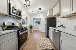 Kitchen featuring sink, light hardwood / wood-style flooring, light stone countertops, appliances with stainless steel finishes, and white cabinetry