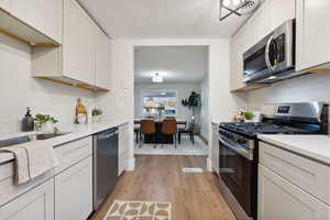 Kitchen with white cabinetry, sink, appliances with stainless steel finishes, and light hardwood / wood-style flooring