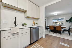 Kitchen with dishwasher, light hardwood / wood-style floors, white cabinetry, and sink