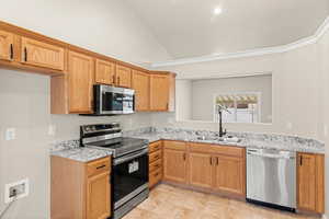 Kitchen with stainless steel appliances, light stone counters, lofted ceiling, and sink