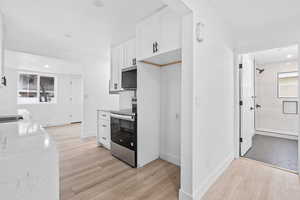 Kitchen featuring white cabinetry, lvp floors, white marble counters, and appliances with stainless steel finishes.