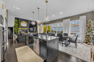 Kitchen with stainless steel dishwasher, dark stone counters, decorative light fixtures, a stone fireplace, and an island with sink