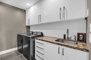 Washroom with cabinets, washing machine and dryer, dark tile patterned floors, and sink