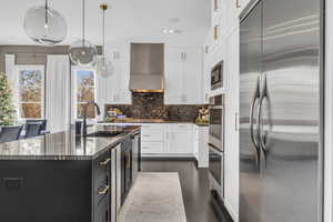 Kitchen featuring sink, stainless steel appliances, wall chimney range hood, pendant lighting, and white cabinets