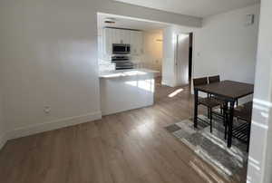 Kitchen with white cabinets, kitchen peninsula, hardwood / wood-style floors, and appliances with stainless steel finishes