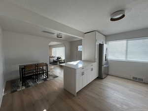 Kitchen with kitchen peninsula, white cabinetry, stainless steel refrigerator, and light hardwood / wood-style flooring