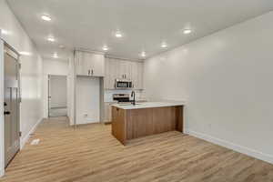 Kitchen featuring light brown cabinets, stainless steel appliances, kitchen peninsula, light hardwood / wood-style floors, and a textured ceiling