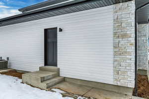 Snow covered property entrance featuring central AC unit