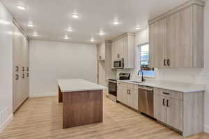 Kitchen with sink, a center island, stainless steel appliances, light hardwood / wood-style floors, and light brown cabinetry