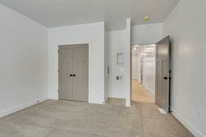 Unfurnished bedroom featuring light carpet, a textured ceiling, and a closet