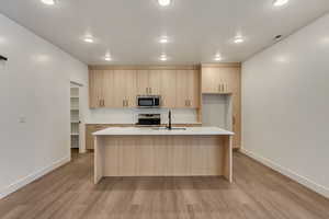 Kitchen with sink, light brown cabinets, stainless steel appliances, light hardwood / wood-style flooring, and a center island with sink