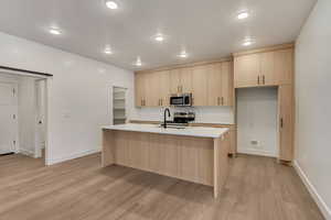 Kitchen with sink, light brown cabinets, light hardwood / wood-style flooring, a center island with sink, and appliances with stainless steel finishes