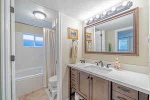 Full bathroom featuring tile patterned floors, vanity, a textured ceiling, shower / bath combo with shower curtain, and toilet