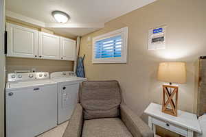 Clothes washing area with cabinets, a textured ceiling, washer and clothes dryer, and light tile patterned flooring