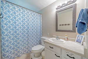 Bathroom featuring a shower with shower curtain, vanity, toilet, and a textured ceiling