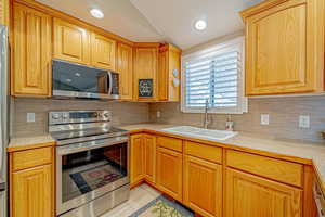 Kitchen with sink, light tile patterned floors, stainless steel appliances, and vaulted ceiling